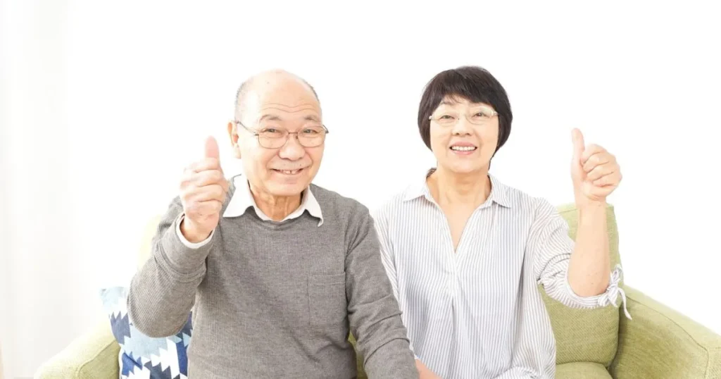 ソファに座って笑顔で親指を立てる高齢者の夫婦